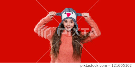Style portrait of teen girl in warm clothing and winter hat isolated on red. Knitted sweater and beanie hat. Trendy fashion outfit in winter. Winter girl child. Knitted accessories 121605102