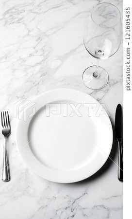 Blank ceramic plate on a marble table with silver cutlery and a wine glass setting for dining 121605438