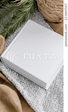 Photorealistic mockup of a hardcover book on textured fabric with natural decor elements 121605507
