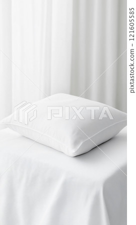 Clean white pillow on a soft surface in a bright, airy room with sheer curtains 121605585