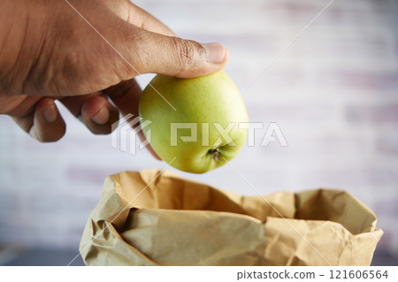 A hand is holding a fresh green apple above a brown paper grocery bag A hand is holding a fresh green apple above a brown paper grocery bag 121606564