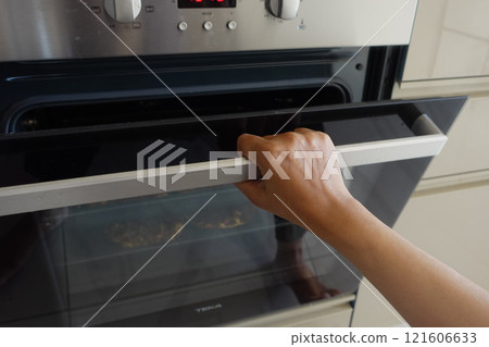 A hand is opening the oven door in preparation for baking delicious food 121606633