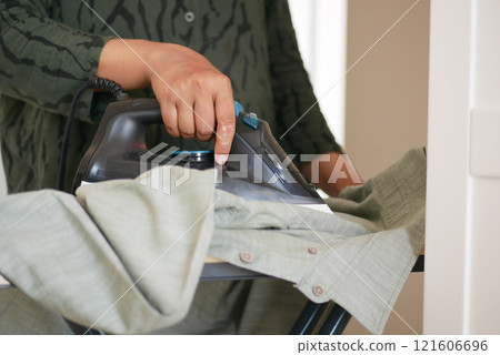 A woman is diligently ironing a shirt using a steam iron for efficiency A woman is diligently ironing a shirt using a steam iron for efficiency 121606696