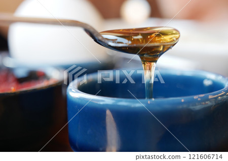 Golden Honey is Dripping Lavishly from the Spoon into the Blue Bowl Golden Honey is Dripping Lavishly from the Spoon into the Blue Bowl 121606714