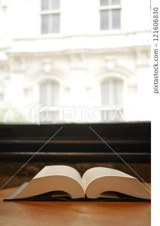 An Open Book Positioned by a Window Allowing for Natural Light to Shine 121606830