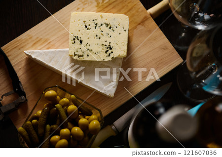 Elegant cheese board with cheese, pickles, and wine glasses on wooden background 121607036