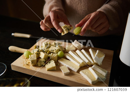 Close-Up of Hands Preparing Cheese and Grapes on a Wooden Board Close-Up of Hands Preparing Cheese and Grapes on a Wooden Board 121607039