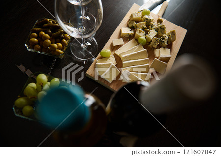 Platter of assorted cheeses with olives, pickles, and wine on a table 121607047