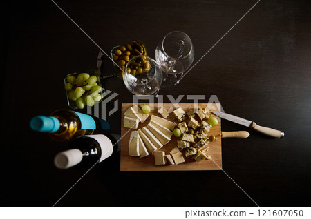 Elegant setup with cheese, wine bottles, and glassware on dark background Elegant setup with cheese, wine bottles, and glassware on dark background 121607050