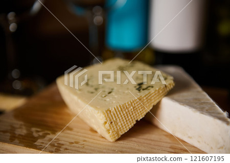 Blocks of assorted artisanal cheeses on a wooden surface under warm lighting 121607195