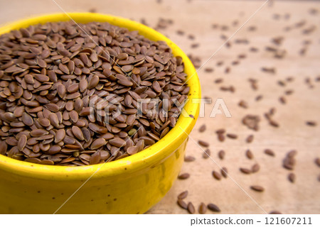 Close-Up Shot of Flaxseeds, Linseeds in a Yellow Bowl with Seeds Spread on a Wooden Table 121607211