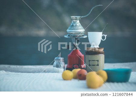 Coffee brewing on a scenic outdoor table with lemons and a jar near a serene body of water at twilight Coffee brewing on a scenic outdoor table with lemons and a jar near a serene body of water at twilight 121607844