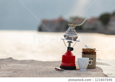 Brewing traditional coffee by the waterfront in a serene coastal setting during early morning light Brewing traditional coffee by the waterfront in a serene coastal setting during early morning light 121607846