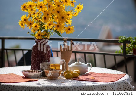 Bright yellow flowers in a vase on a table set with colorful dishes and a scenic backdrop creates a warm atmosphere for morning tea on a sunny day Bright yellow flowers in a vase on a table set with colorful dishes and a scenic backdrop creates a warm atmosphere for morning tea on a sunny day 121607851