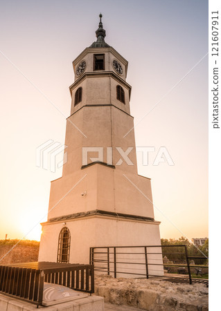The Clock Tower and Gate stand majestically at Kalemegdan Fortress, illuminated by the warm glow of the sunset, casting long shadows and highlighting the ancient architecture. 121607911