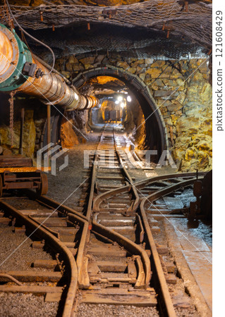 A historic mine shaft in Jachymov, Czechia reveals rusty tracks and wooden beams. Dim lights illuminate the underground space, showcasing remnants of mining activity in this unique location. A historic mine shaft in Jachymov, Czechia reveals rusty tracks and wooden beams. Dim lights illuminate the underground space, showcasing remnants of mining activity in this unique location. 121608429