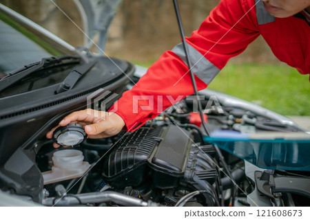 A mechanic is checking the engine coolant level under the hood of a car 121608673