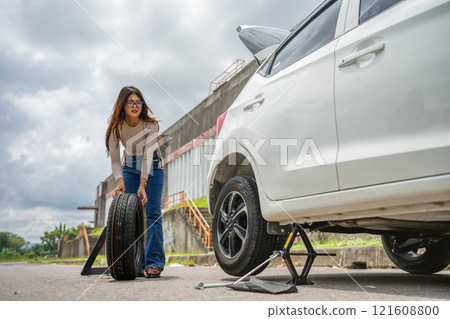 A woman is skillfully changing a tire on a white car in an outdoor setting A woman is skillfully changing a tire on a white car in an outdoor setting 121608800