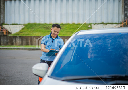 A man is writing on a clipboard by his parked car, completing his checklist A man is writing on a clipboard by his parked car, completing his checklist 121608815