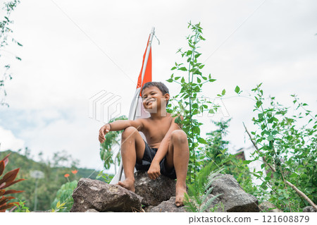 boy sitting on rock with stick with Indonesian flag on nature background 121608879