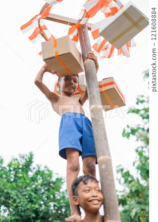 boy stands on friend's shoulders reaching for prize during betel nut climbing boy stands on friend's shoulders reaching for prize during betel nut climbing 121608884