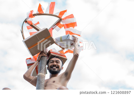 smiling man reaching for the prize box in a betel nut climbing smiling man reaching for the prize box in a betel nut climbing 121608897