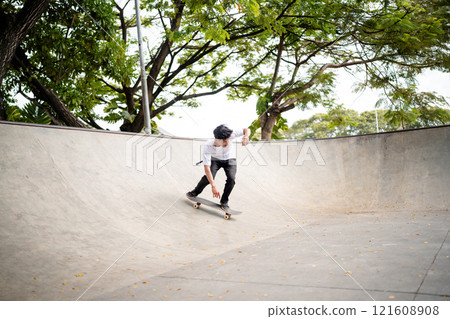 A Skater Skillfully Performing a Trick in a Spacious Concrete Bowl at a Local Skate Park 121608908