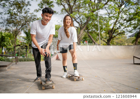 Two close friends are having a great time skateboarding together at a sunny skate park 121608944