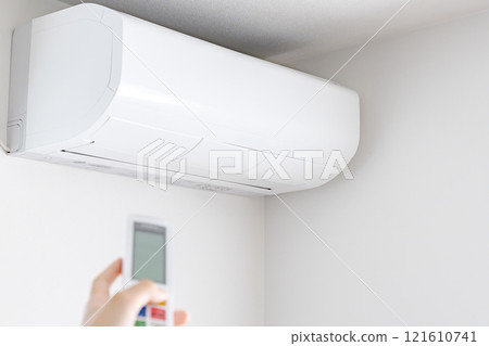 A large white air conditioner and a woman's left hand with a remote control 121610741