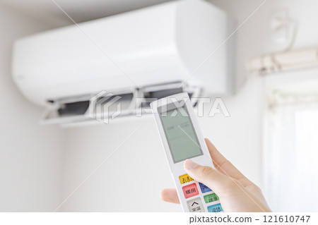Female hand operating the remote control of the air conditioner 121610747