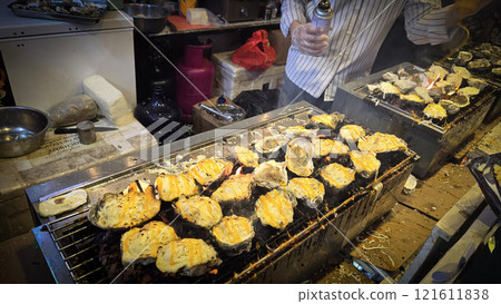 street vendor uses a torch flame to prepare delicious grilled oyster with flair and skill, showcasing the vibrant atmosphere of bustling night Thai markets 121611838