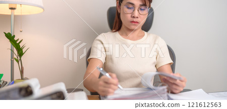 Asian woman reading financial report, female businesswoman sign contract or writing documents paper at home or office late night. Overworked, work hard and business concept Asian woman reading financial report, female businesswoman sign contract or writing documents paper at home or office late night. Overworked, work hard and business concept 121612563