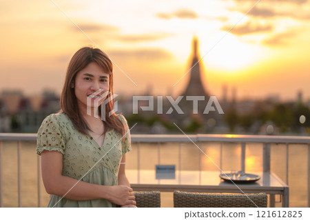tourist woman enjoys view to Wat Arun Temple in sunset, Traveler visits Temple of Dawn near Chao Phraya river from rooftop bar. Landmark and Travel destination in Bangkok, Thailand and Southeast Asia 121612825