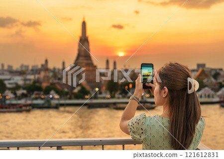 tourist woman enjoys view to Wat Arun Temple in sunset, Traveler take photo to Temple of Dawn by smartphone from rooftop bar. Landmark and Travel destination in Bangkok, Thailand and Southeast Asia tourist woman enjoys view to Wat Arun Temple in sunset, Traveler take photo to Temple of Dawn by smartphone from rooftop bar. Landmark and Travel destination in Bangkok, Thailand and Southeast Asia 121612831
