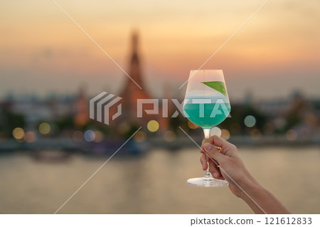 tourist hand shows cocktail glass during enjoy view to Wat Arun Temple in sunset, Traveler visits Temple of Dawn near from rooftop bar. Travel destination in Bangkok, Thailand and Southeast Asia tourist hand shows cocktail glass during enjoy view to Wat Arun Temple in sunset, Traveler visits Temple of Dawn near from rooftop bar. Travel destination in Bangkok, Thailand and Southeast Asia 121612833