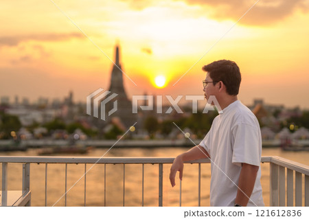 tourist man enjoys view to Wat Arun Temple in sunset, Traveler visits Temple of Dawn near Chao Phraya river from rooftop bar. Landmark and Travel destination in Bangkok, Thailand and Southeast Asia 121612836