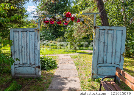 A creative garden entrance made of two old decorative doors forming an archway, adorned with flowers. The setting highlights creativity, upcycling, and handmade A creative garden entrance made of two old decorative doors forming an archway, adorned with flowers. The setting highlights creativity, upcycling, and handmade 121615079