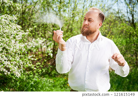 Man allergic using medical nasal drops, suffering from seasonal allergy at spring in blossoming garden. Handsome man examining nasal spray near blooming tree outdoors. Spring allergy concept. Man allergic using medical nasal drops, suffering from seasonal allergy at spring in blossoming garden. Handsome man examining nasal spray near blooming tree outdoors. Spring allergy concept. 121615149