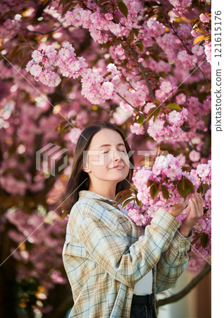 Woman allergic enjoying after treatment from seasonal allergy. Portrait of happy beautiful woman smiling with eyes closed in front of blooming sakura tree at springtime. Spring allergy concept. Woman allergic enjoying after treatment from seasonal allergy. Portrait of happy beautiful woman smiling with eyes closed in front of blooming sakura tree at springtime. Spring allergy concept. 121615176