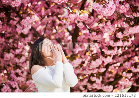 Woman allergic suffering from seasonal allergy at spring in blossoming garden at springtime. Young woman having runny nose in front of blooming tree. Spring allergy concept Woman allergic suffering from seasonal allergy at spring in blossoming garden at springtime. Young woman having runny nose in front of blooming tree. Spring allergy concept 121615178