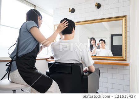 A female hairdresser and a male customer checking and consulting their hair in front of a mirror at a beauty salon A female hairdresser and a male customer checking and consulting their hair in front of a mirror at a beauty salon 121615427