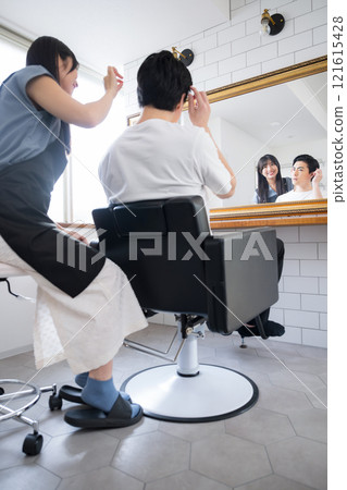 A female hairdresser and a male customer checking and consulting their hair in front of a mirror in a beauty salon. A female hairdresser and a male customer checking and consulting their hair in front of a mirror in a beauty salon. 121615428