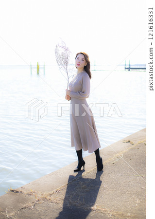 A beautiful lady standing by the water under a clear autumn sky. A beautiful lady standing by the water under a clear autumn sky. 121616331
