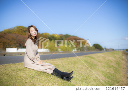 A beautiful lady standing by the water under a clear autumn sky. 121616457