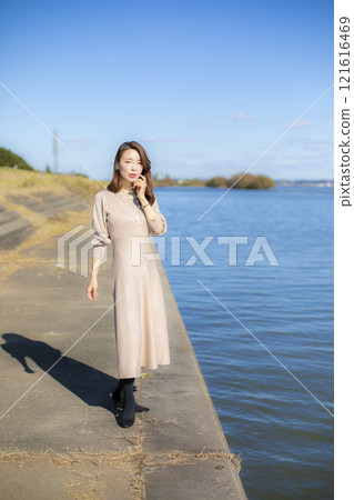 A beautiful lady standing by the water under a clear autumn sky. 121616469