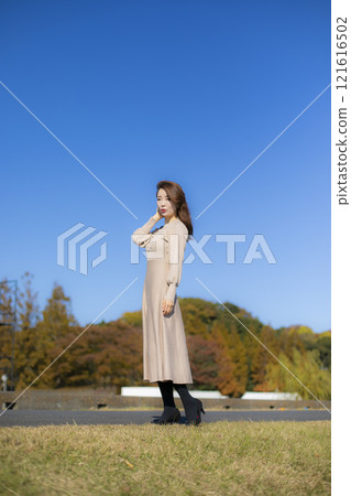A beautiful lady standing by the water under a clear autumn sky. 121616502