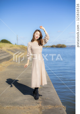 A beautiful lady standing by the water under a clear autumn sky. 121616516