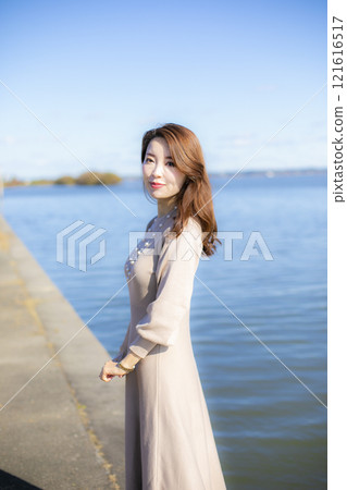 A beautiful lady standing by the water under a clear autumn sky. 121616517