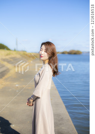 A beautiful lady standing by the water under a clear autumn sky. 121616518