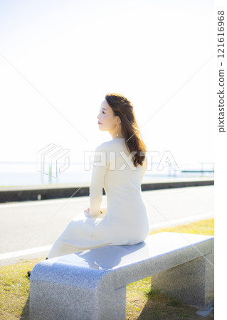 A beautiful lady standing by the water under a clear autumn sky. 121616968